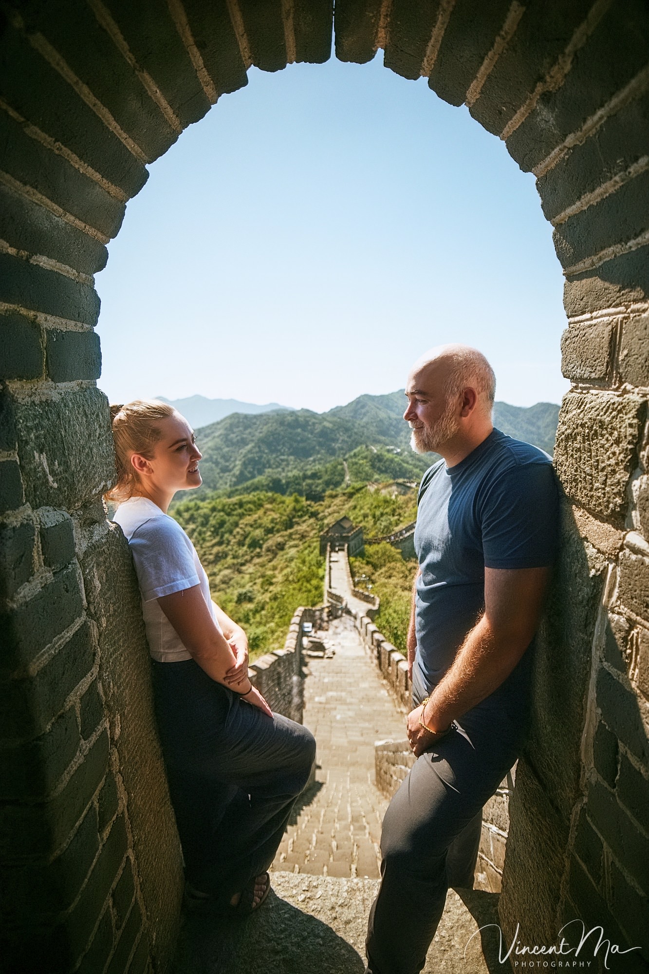 An American couple posing for romantic pictures against the backdrop of Mutianyu Great Wall in Beijing, China. The Great Wall winds through the mountains, and the couple shows their love in the photos