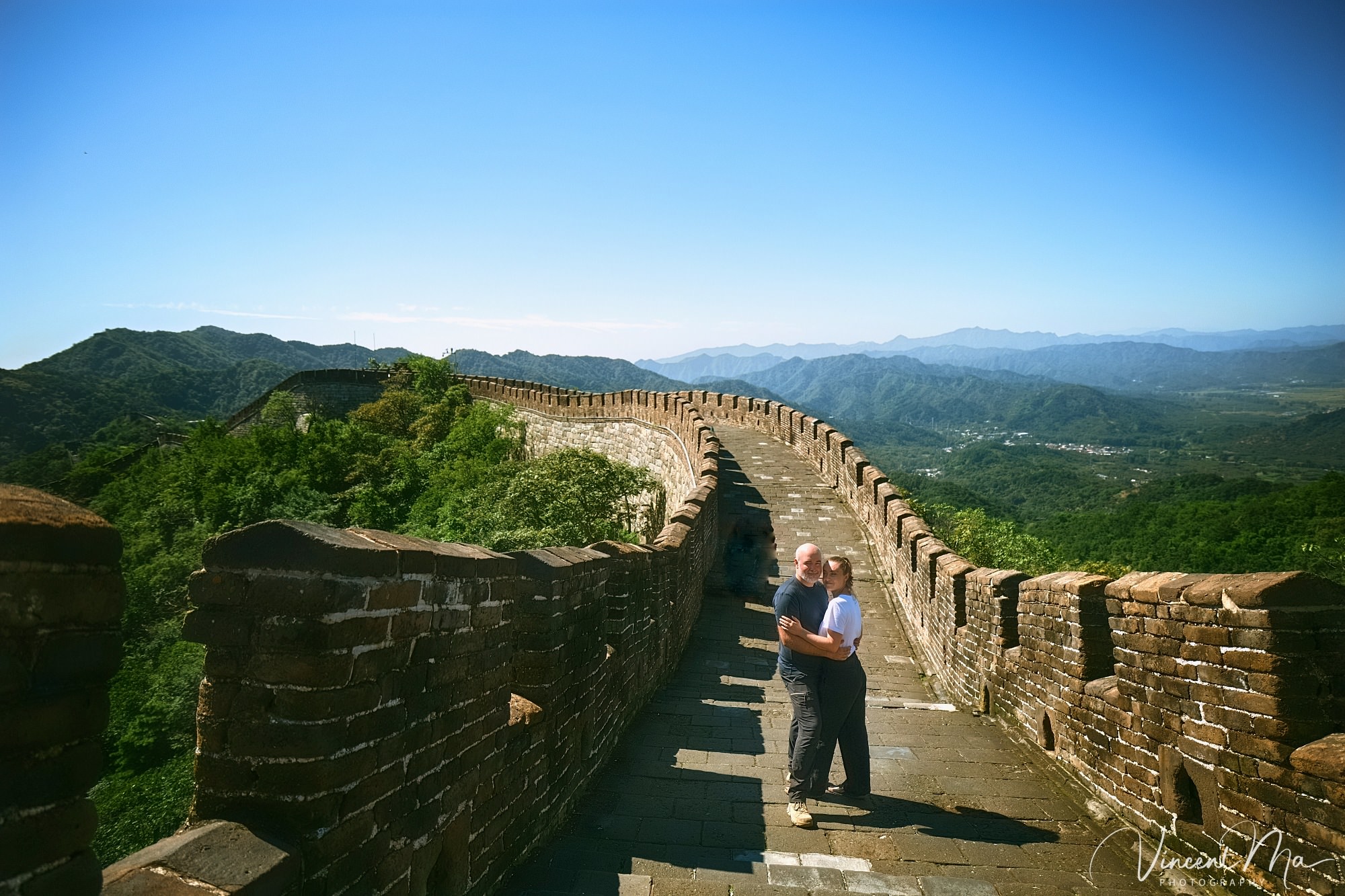 An American couple posing for romantic pictures against the backdrop of Mutianyu Great Wall in Beijing, China. The Great Wall winds through the mountains, and the couple shows their love in the photos