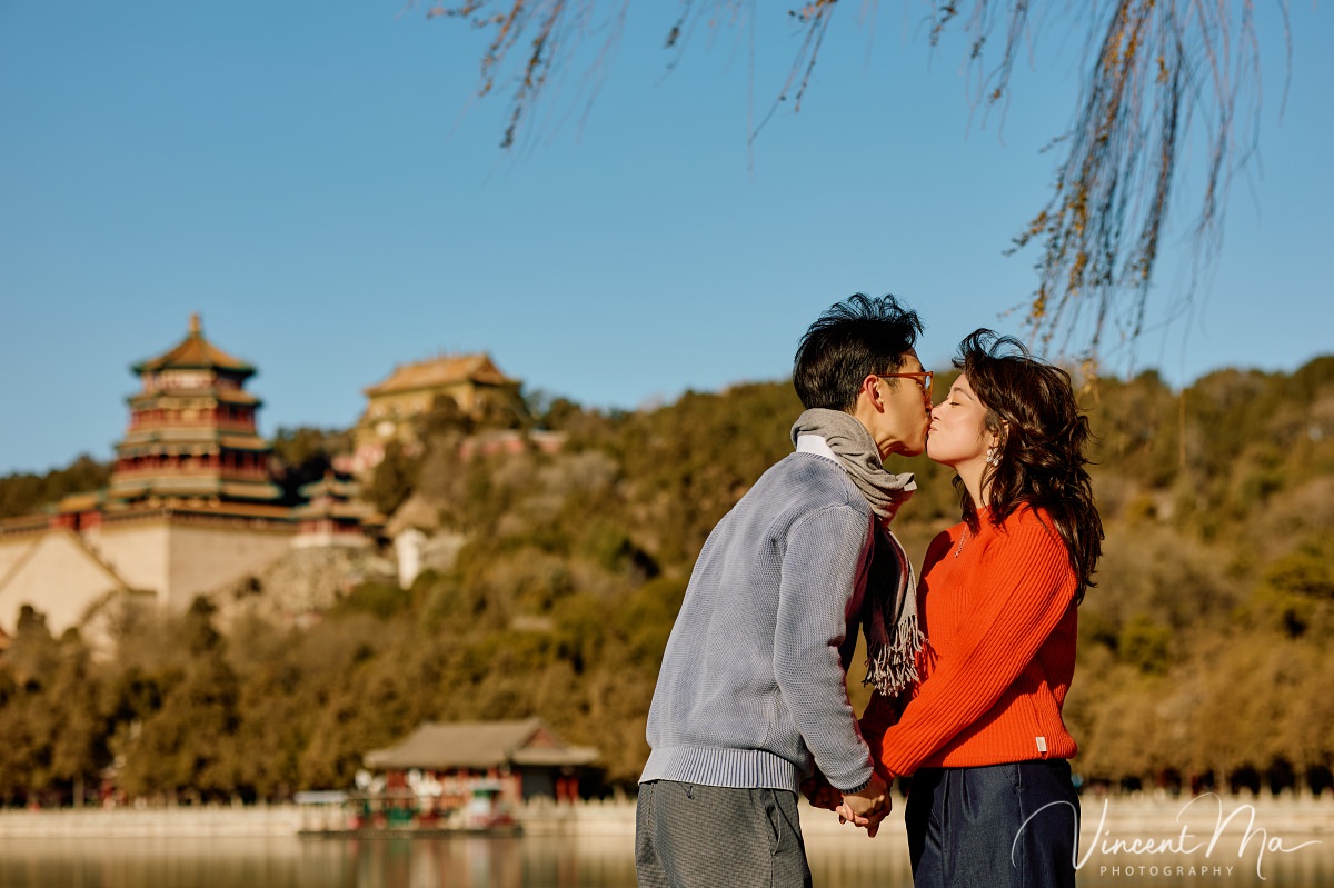 Couple sharing a romantic kiss with the Tower of Buddhist Incense in the background at the Summer Palace, Beijing. Winter engagement photography with clear blue sky