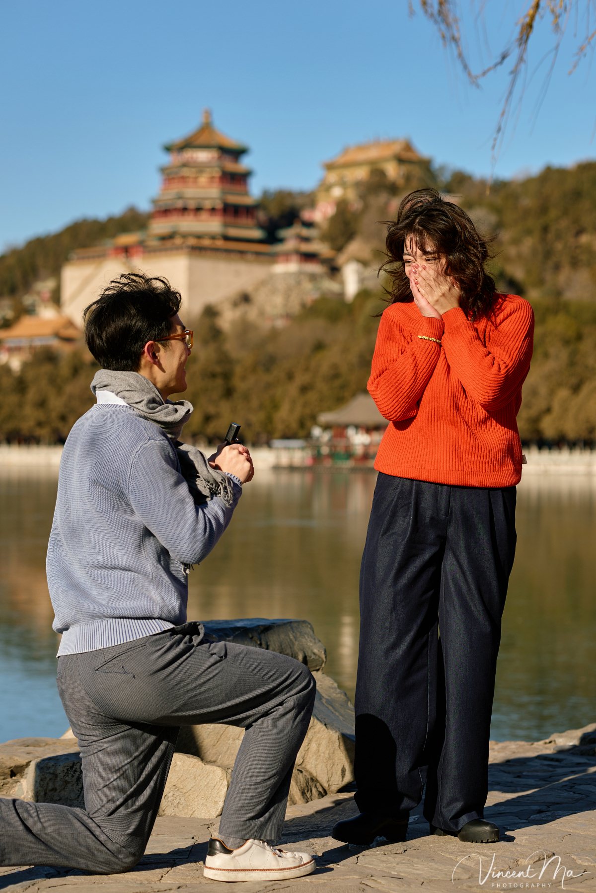 Couple sharing a romantic kiss with the Tower of Buddhist Incense in the background at the Summer Palace, Beijing. Winter engagement photography with clear blue sky