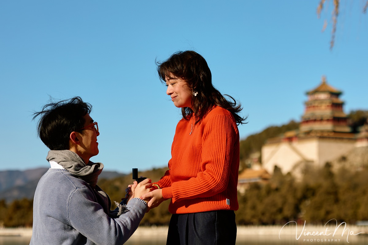 Couple sharing a romantic kiss with the Tower of Buddhist Incense in the background at the Summer Palace, Beijing. Winter engagement photography with clear blue sky