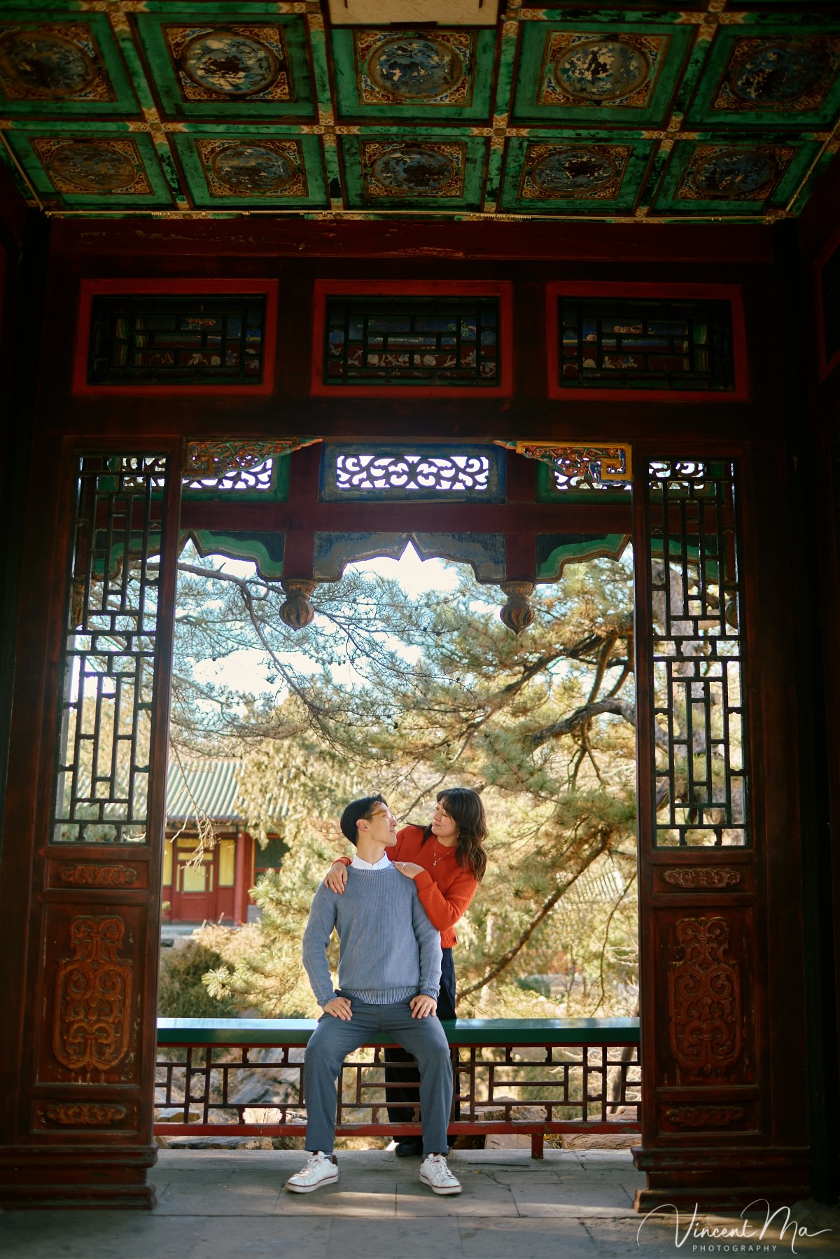 Beijing engagement photography. Couple looking at each other lovingly on a stone bridge at the Summer Palace. Traditional Chinese pavilion and winter reeds in the background.
