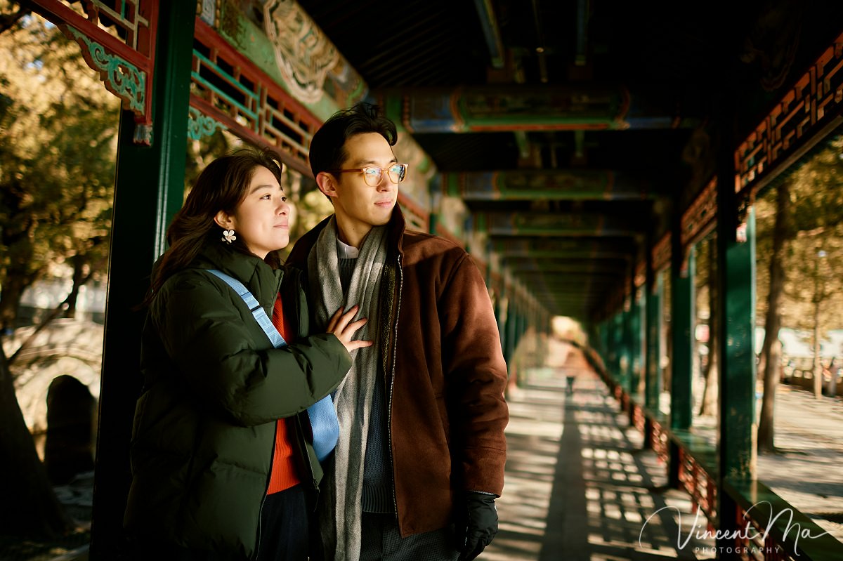 Beijing engagement photography. Engaged couple standing inside the famous Long Corridor at the Summer Palace, Beijing. Dramatic winter sunlight creates rhythmic shadows on the floor and pillars.