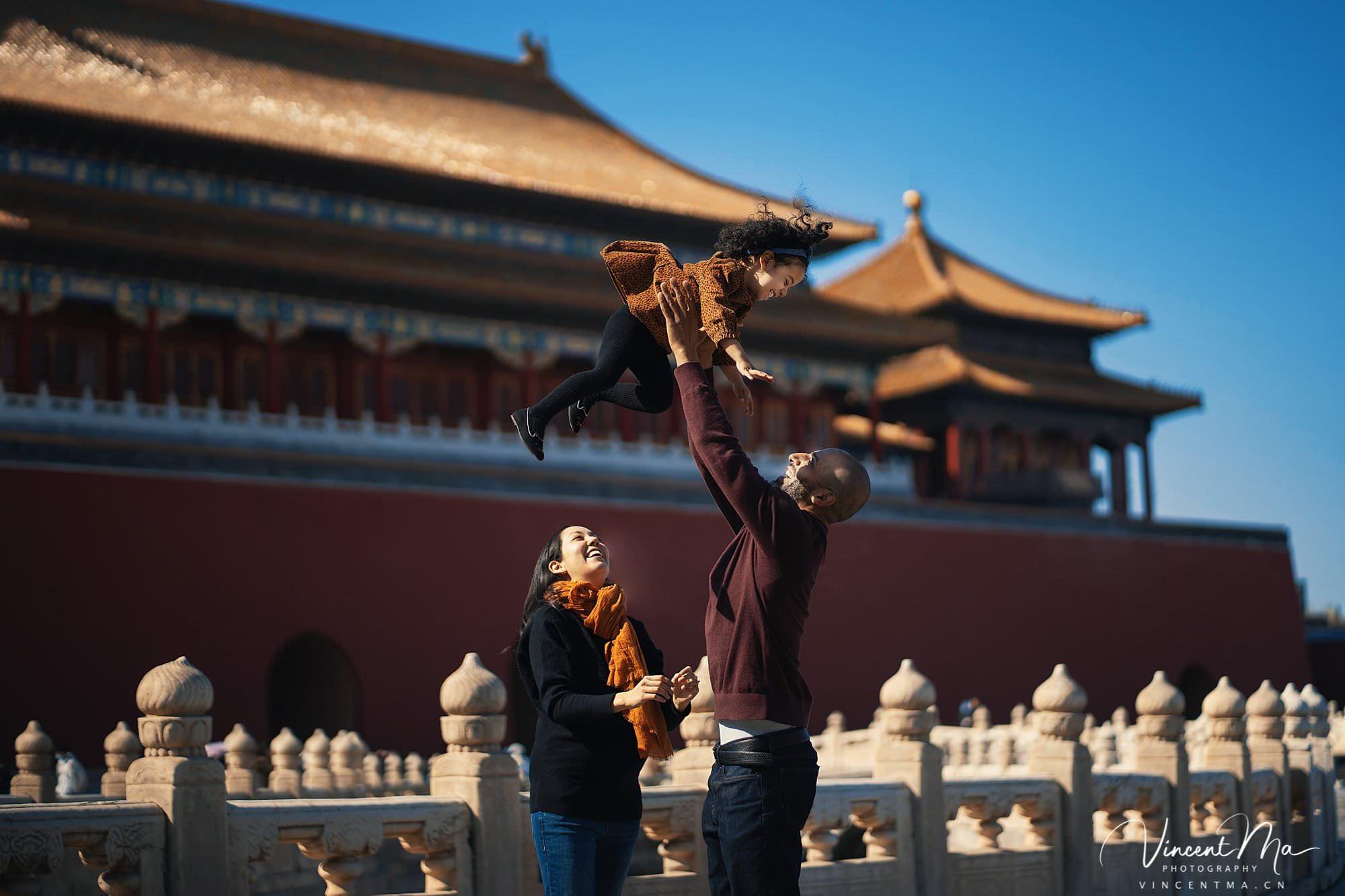 US family of three with toddler laughing in front of the Hall of Supreme Harmony at Forbidden City, blue sky and no tourists.Family photography by Vincent Ma