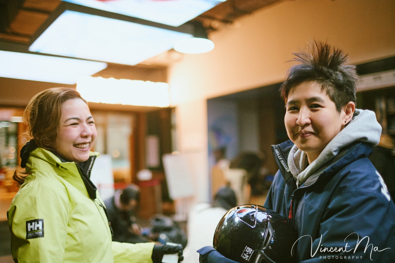 Same-sex couple snowboarding together in powder snow wearing cute turtle and avocado protective gear at a Chongli ski resort.
