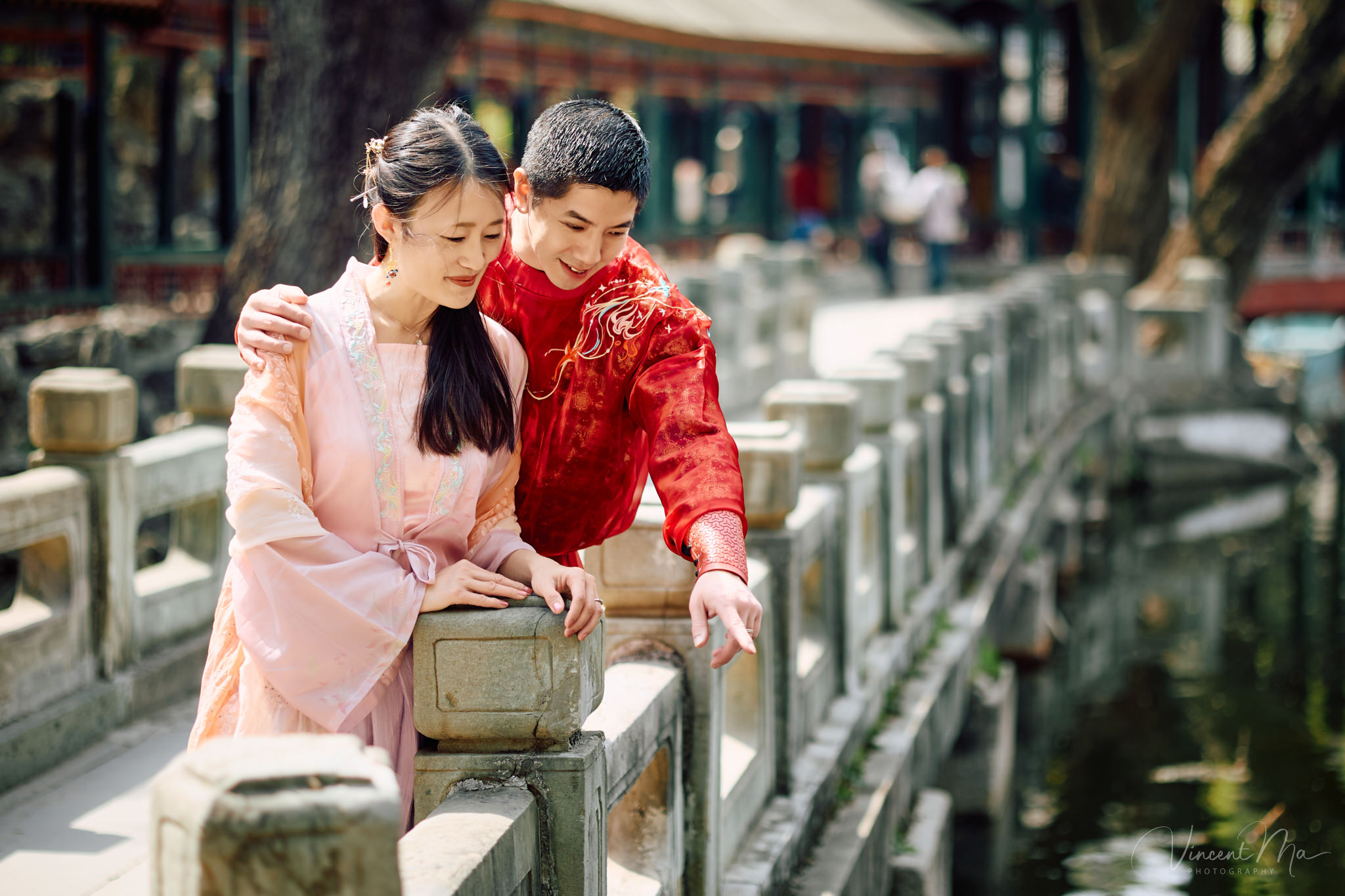 Family of four sitting by the lake under green weeping willows and spring cherry blossoms at the Summer Palace.