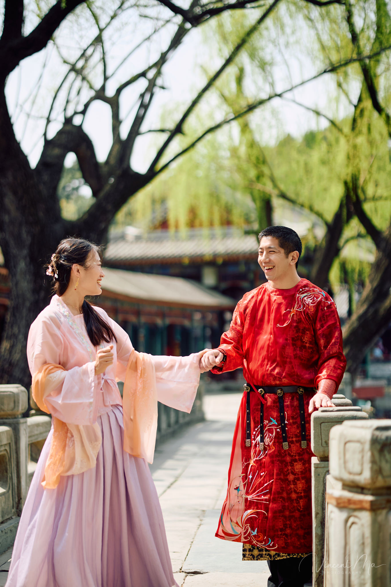 Family of four sitting by the lake under green weeping willows and spring cherry blossoms at the Summer Palace.
