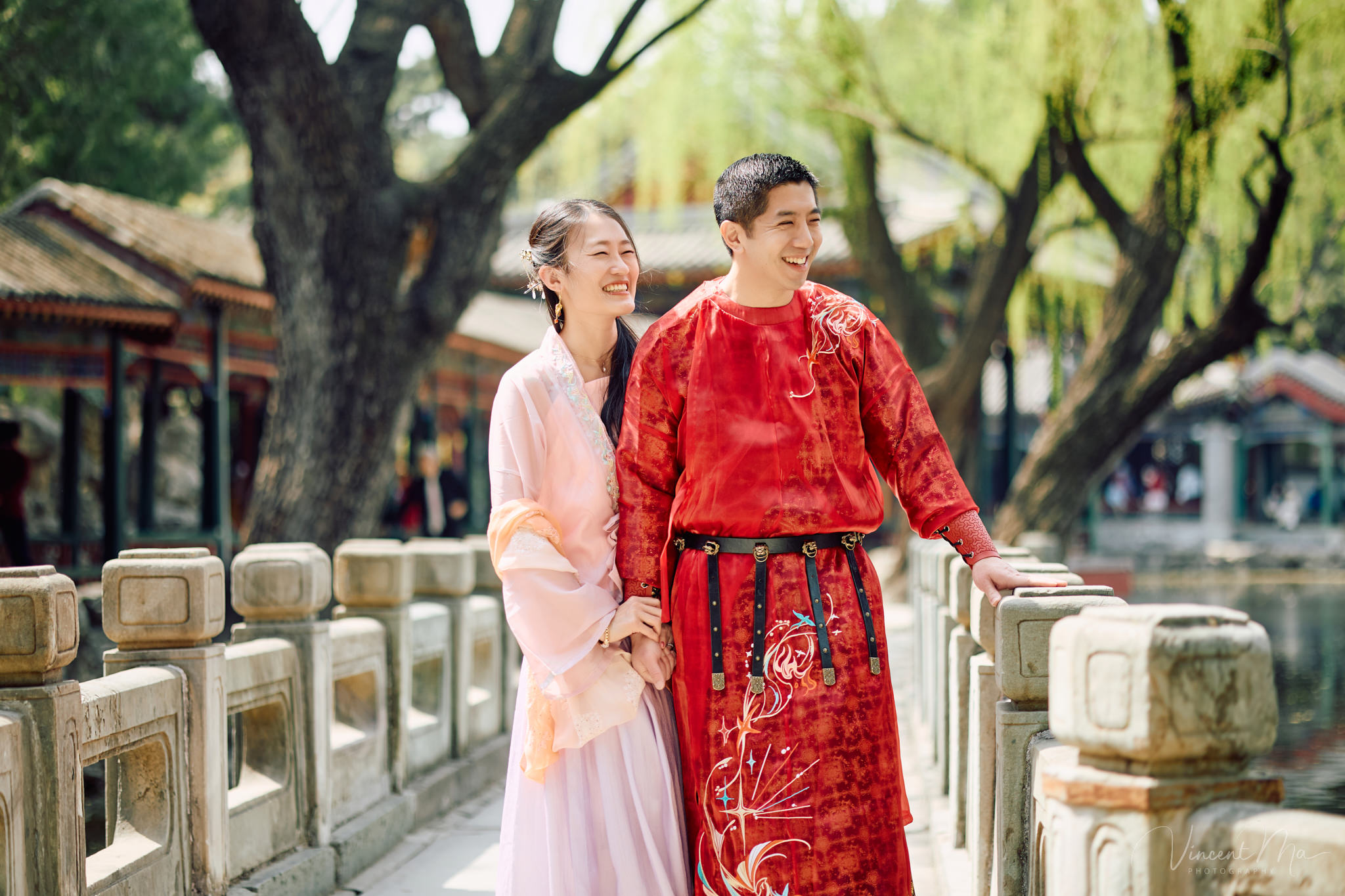 Family of four sitting by the lake under green weeping willows and spring cherry blossoms at the Summer Palace.