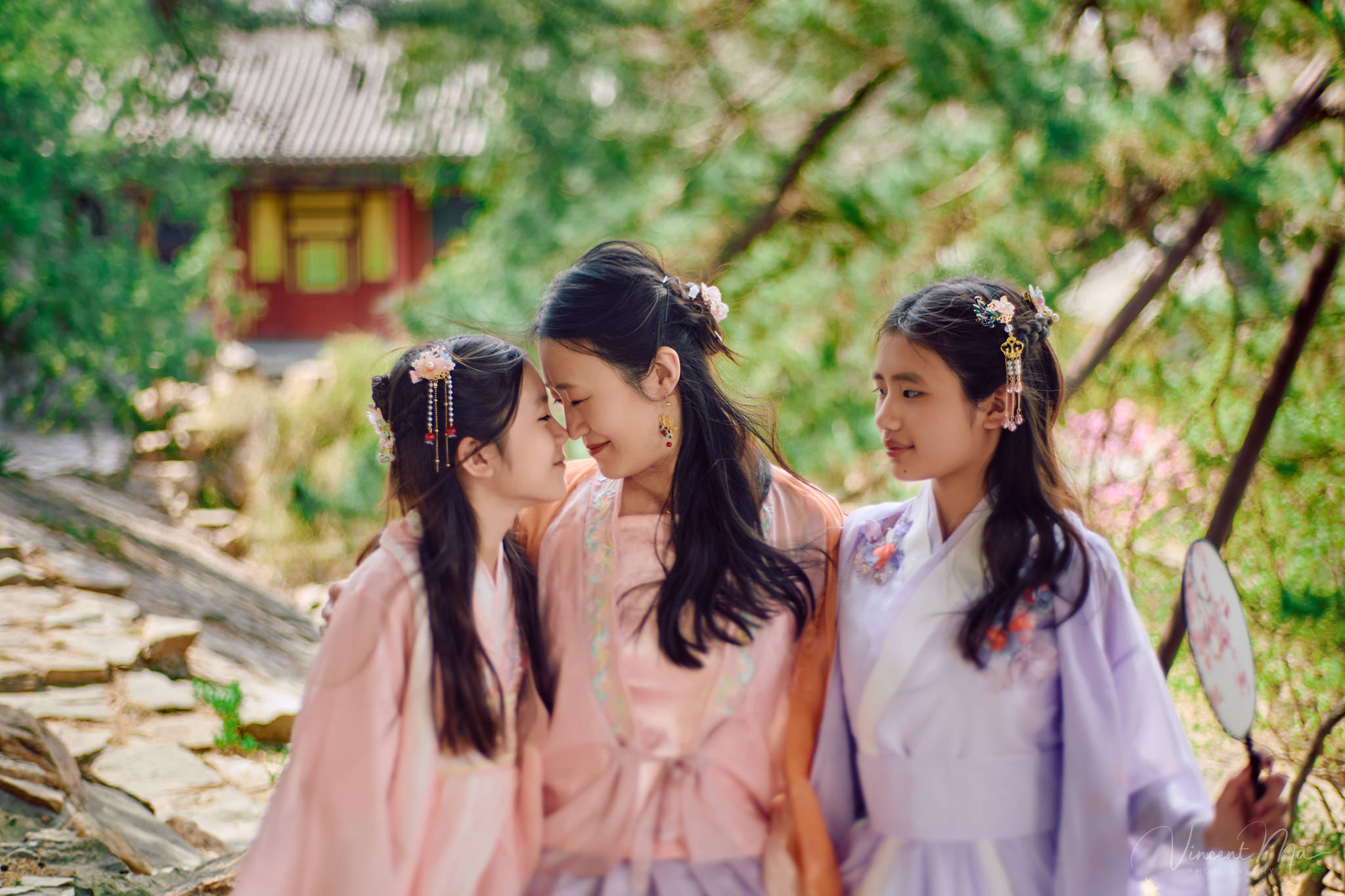Mother and daughter in pink Hanfu costumes playing with traditional fans under blooming spring peach blossoms at the Summer Palace.