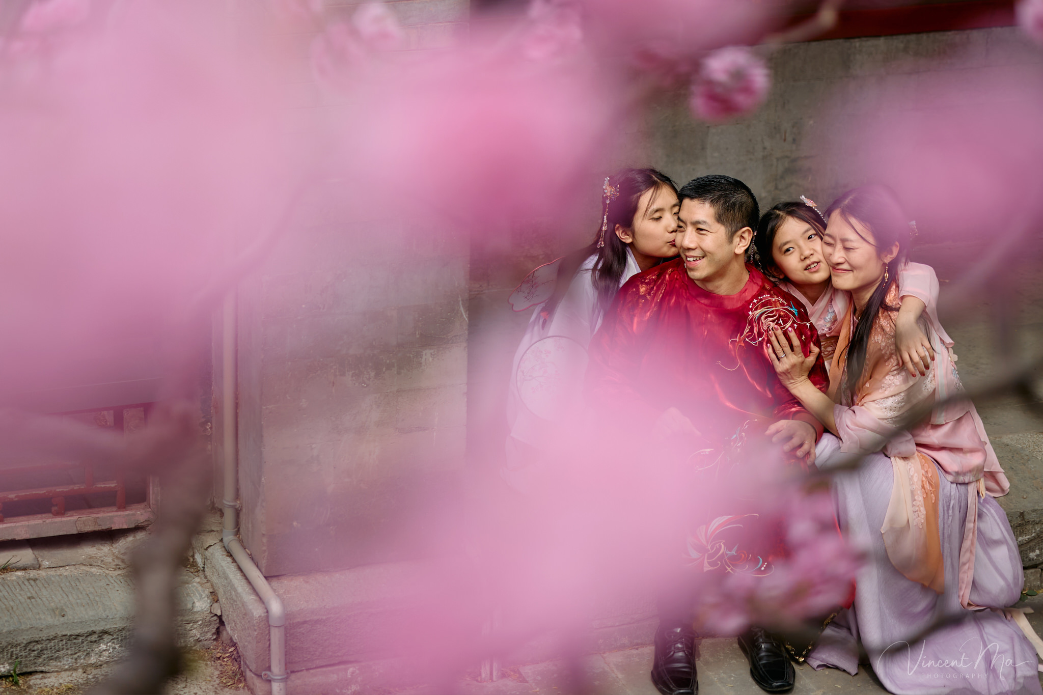 Mother and daughter in pink Hanfu costumes playing with traditional fans under blooming spring peach blossoms at the Summer Palace.
