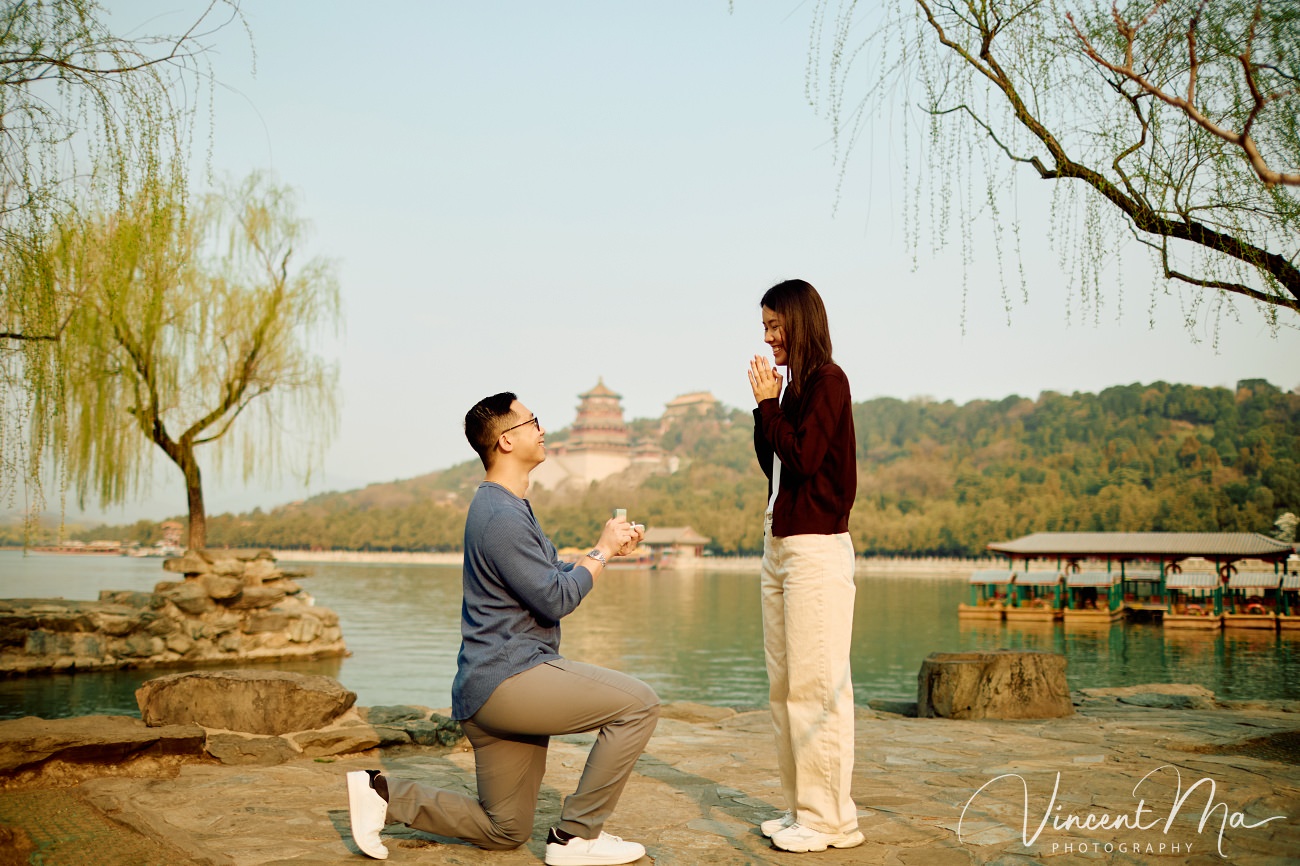 Breathtaking moment of a secret proposal at the Summer Palace, Beijing. A man on one knee amidst spring flowers and ancient imperial architecture. Captured by Beijing photographer Vincent Ma.