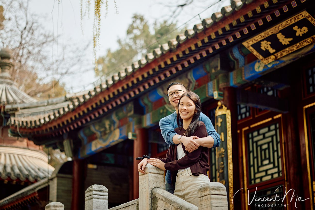 A cinematic capture of a secret proposal at the Summer Palace, Beijing. The couple is framed by blooming cherry blossoms and magnolias with the Tower of Buddhist Incense in the background. Professional photography by Vincent Ma for an American couple's first trip to China.