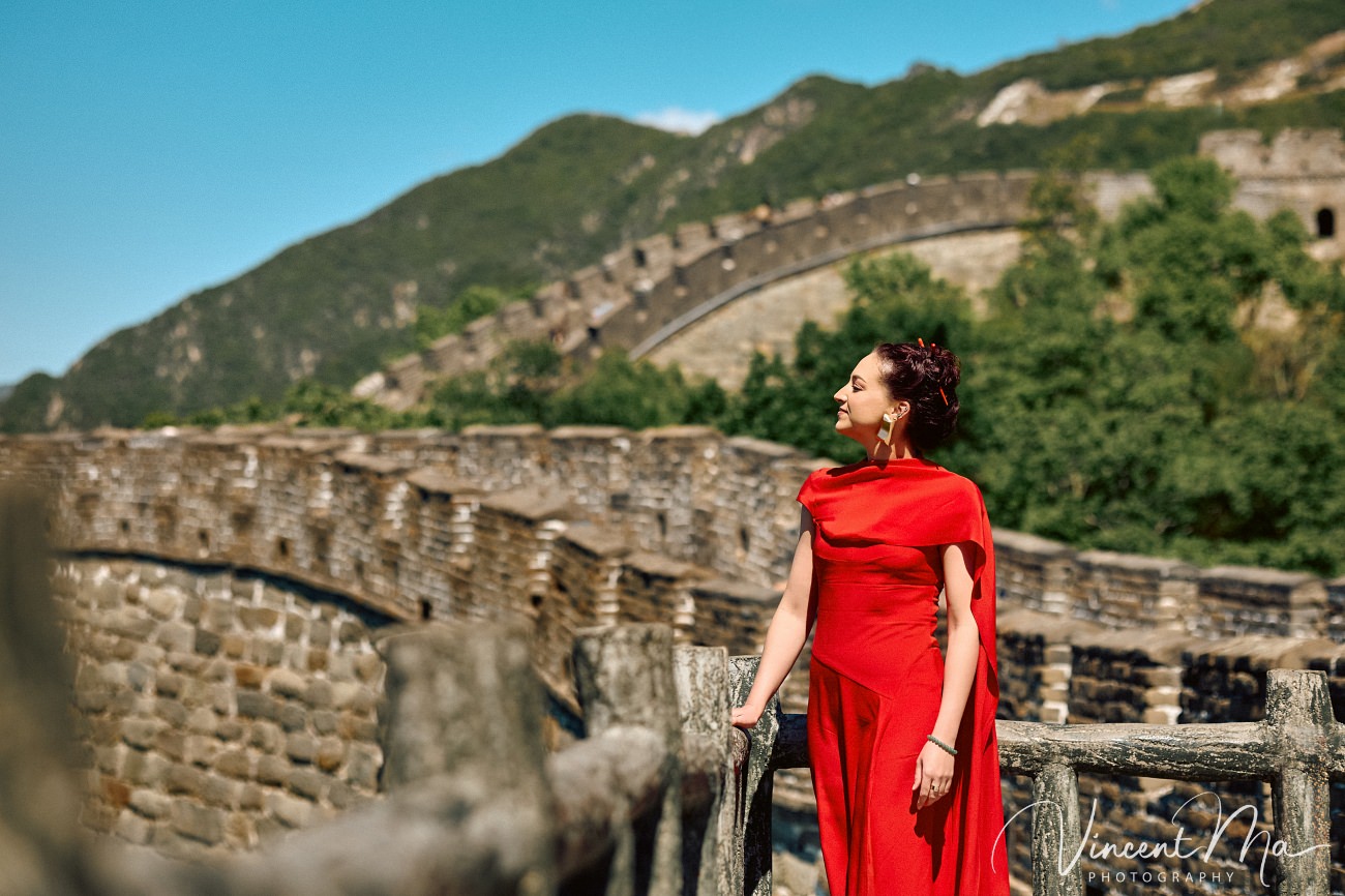 Wide-angle cinematic fashion shot at the empty Mutianyu Great Wall. A solo traveler in a flowing dress silhouetted against the vast mountain ridges of Beijing.