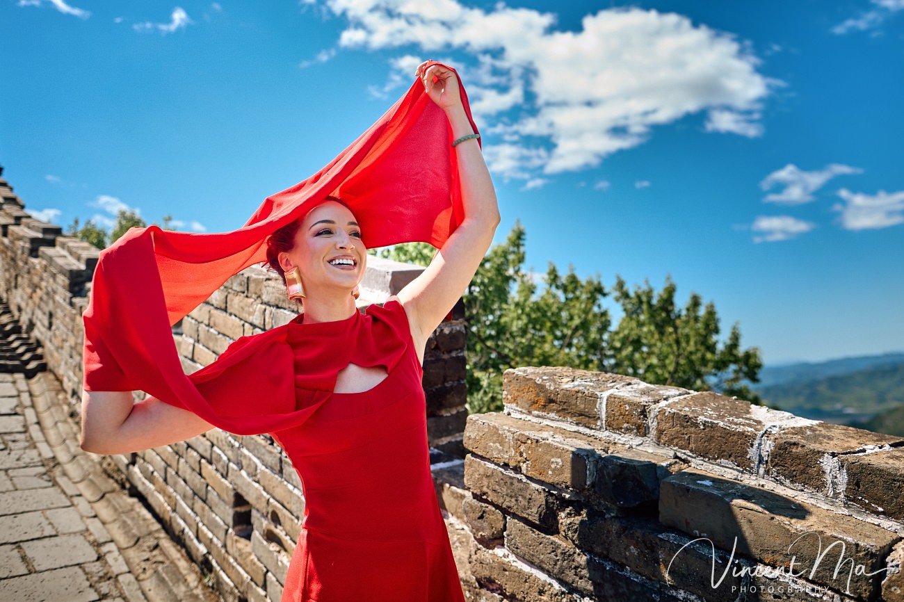 Wide-angle cinematic fashion shot at the empty Mutianyu Great Wall. A solo traveler in a flowing dress silhouetted against the vast mountain ridges of Beijing.