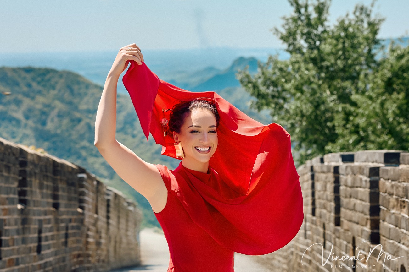 Wide-angle cinematic fashion shot at the empty Mutianyu Great Wall. A solo traveler in a flowing dress silhouetted against the vast mountain ridges of Beijing.