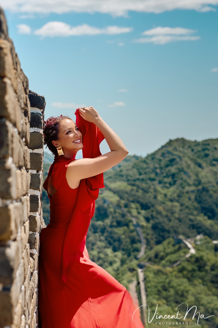 Wide-angle cinematic fashion shot at the empty Mutianyu Great Wall. A solo traveler in a flowing dress silhouetted against the vast mountain ridges of Beijing.