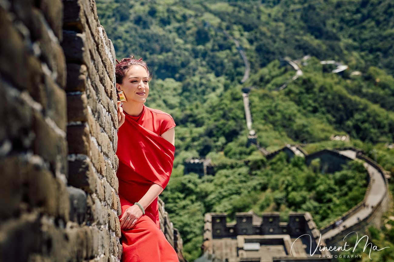 Wide-angle cinematic fashion shot at the empty Mutianyu Great Wall. A solo traveler in a flowing dress silhouetted against the vast mountain ridges of Beijing.