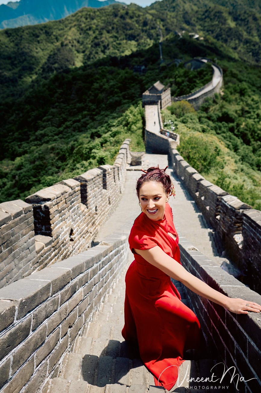 Wide-angle cinematic fashion shot at the empty Mutianyu Great Wall. A solo traveler in a flowing dress silhouetted against the vast mountain ridges of Beijing.