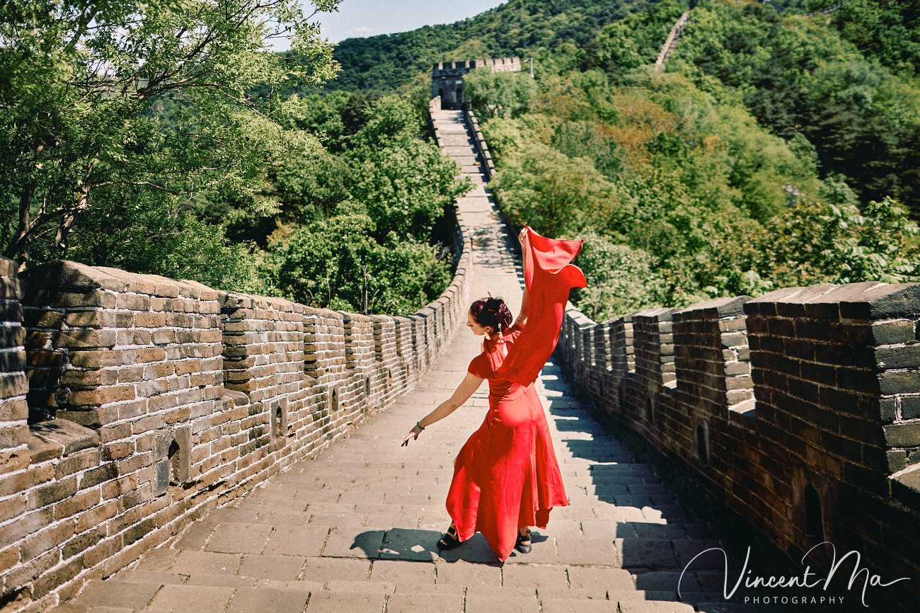Wide-angle cinematic fashion shot at the empty Mutianyu Great Wall. A solo traveler in a flowing dress silhouetted against the vast mountain ridges of Beijing.